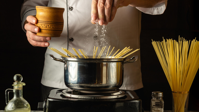 A person salting pasta water with spaghetti noodles standing around edges of pot