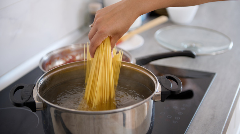 A person adding dry spaghetti pasta to a pot of water