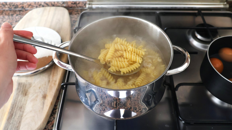 A person lifting a spoonful of spiral pasta from a pot of boiling water