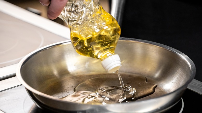 Person pouring cooking oil into a skillet