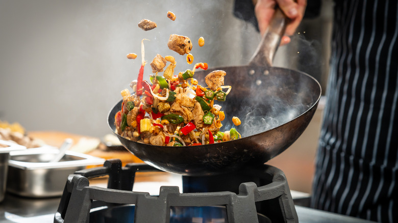 Person tossing vegetables in a wok