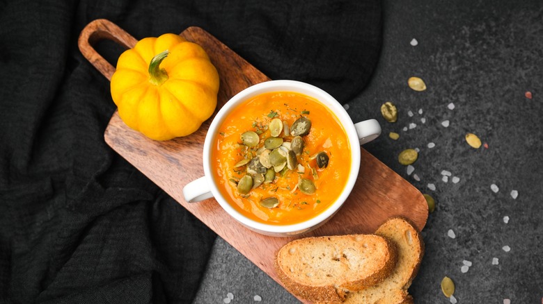White bowl of pumpkin soup garnished with pumpkin seeds and accompanied by toast points