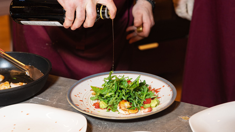 Balsamic vinegar being drizzled over arugula salad