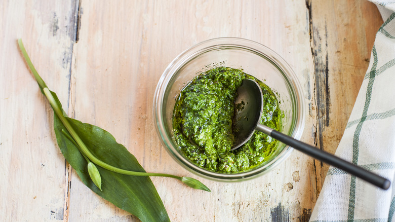 Homemade pesto in a glass bowl, with a leaf next to it