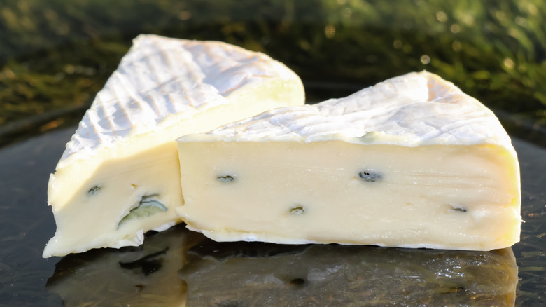 Two wedges of Cambozola cheese on a black marble platter