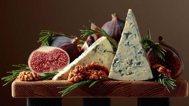 Two wedges of blue cheese on a board with figs, walnuts, and rosemary
