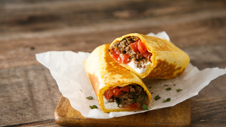 A beef burrito cut in half on a wooden cutting board