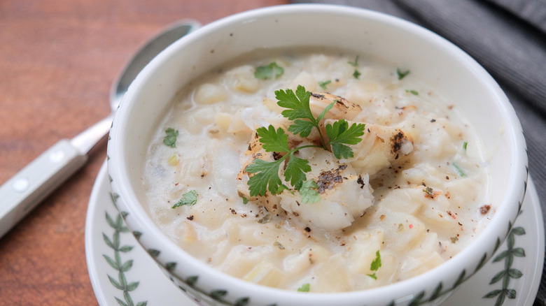 Finnan haddie/Cullen skink chowder in a white bowl with green vines painted on, parsley garnish, and a spoon, on a brown surface