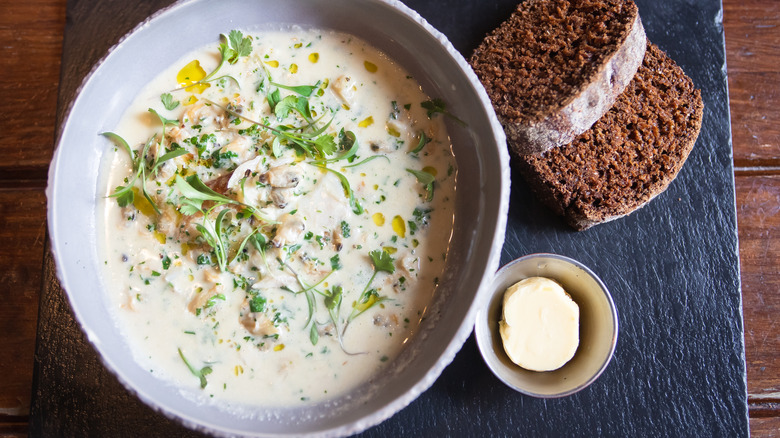 Large white bowl of Irish fish chowder on slate platter with two slices of brown bread and a small dish of butter