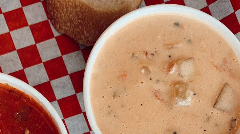 Two white bowls of clam chowder, one pink, one red, on a red and white checked tablecloth, with a crust of bread