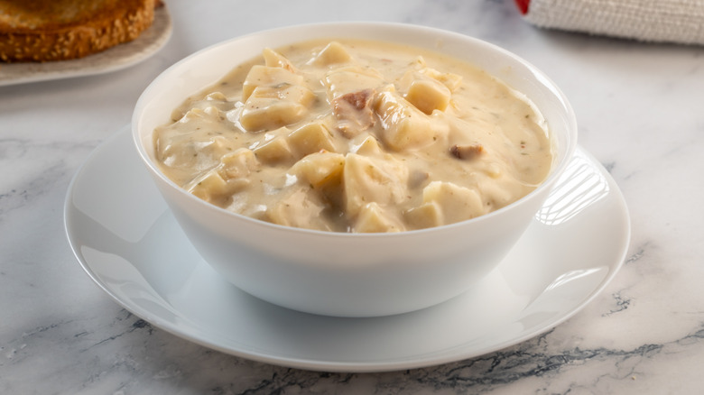 White bowl and saucer with creamy potato chowder, a bit of toast, on a marble surface