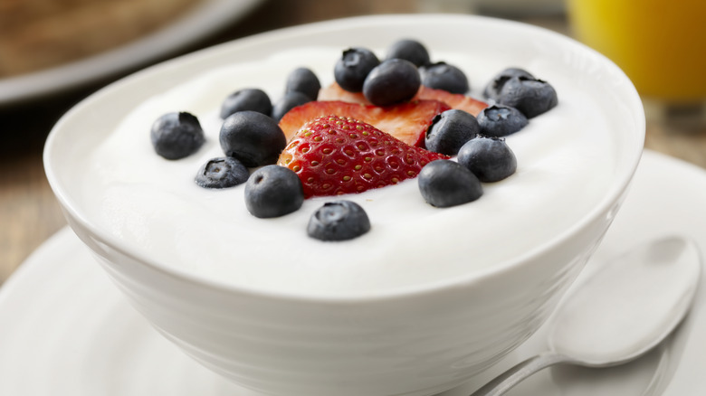 Bowl of yogurt topped with sliced strawberries and blueberries
