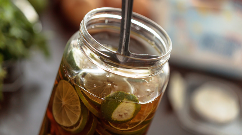 Glass jar filled with fresh lime slices preserved in honey, creating a homemade honey lime infusion