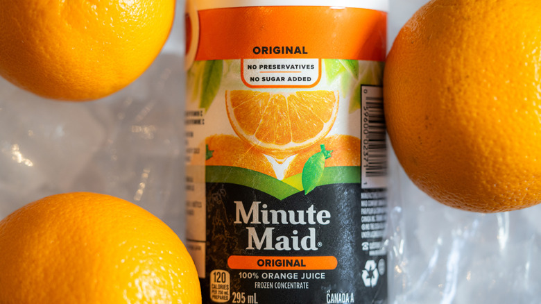 A can of Minute Maid original frozen orange juice concentrate surrounded by fresh oranges