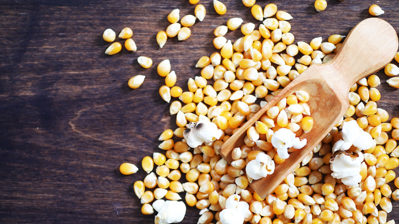Wooden scooper filled with popcorn kernels and popped corn