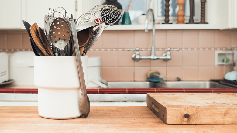 A pot of utensils on a butcher block countertop with a sink in the background