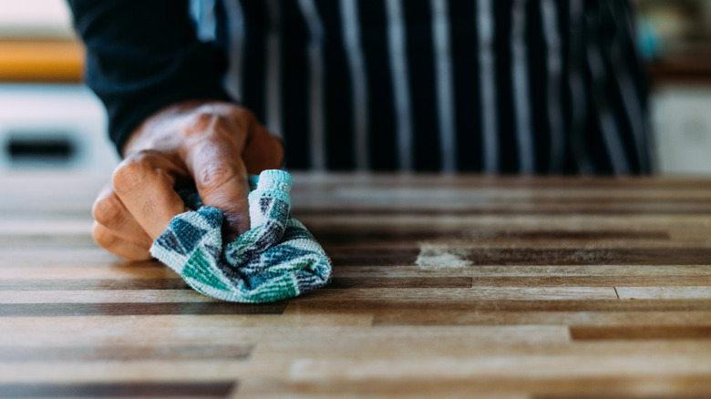 A person wearing an apron and cleaning butcher block with a blue cloth