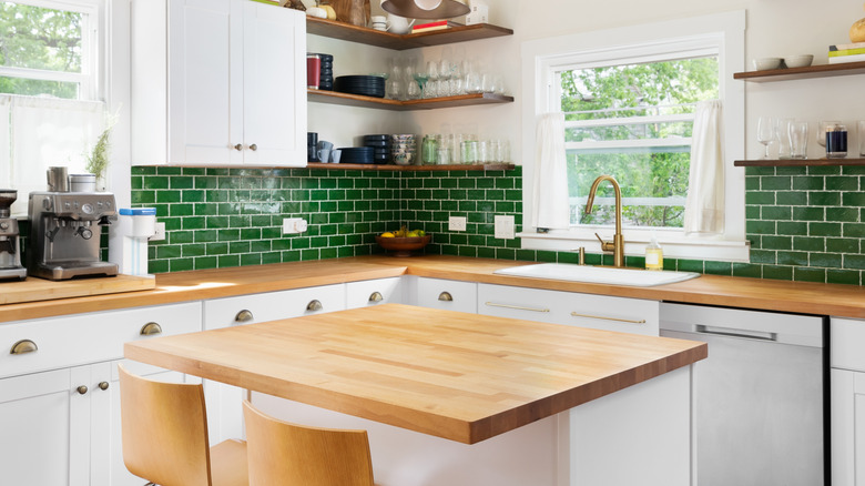 A butcher block kitchen island in a white kitchen with green backsplash tiles