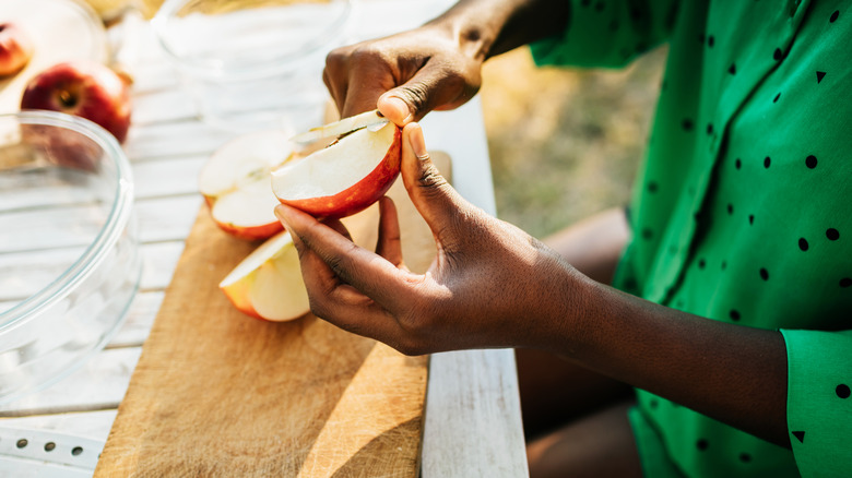 Woman's hands slicing an apple over a cutting board on an outdoor table