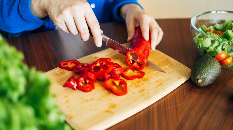 Closeup of a person's hands cutting a bell pepper on a cutting board