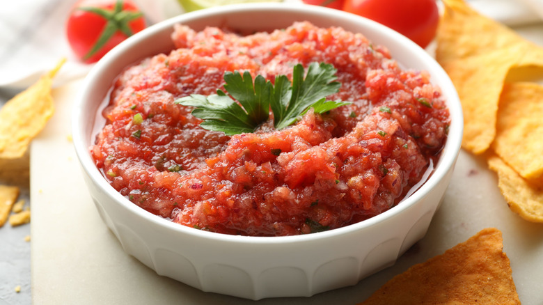 Bowl of salsa surrounded by tomatoes and tortilla chips