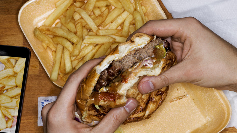 A person holding a burger with French fries on the side