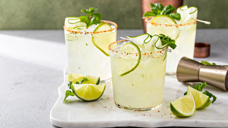 Three cucumber cocktails on a cutting board garnished with lime