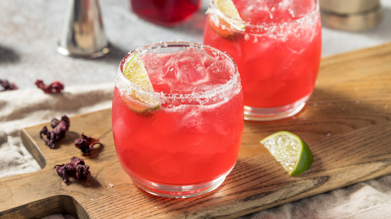 Two hibiscus cocktails on a cutting board garnished with lime