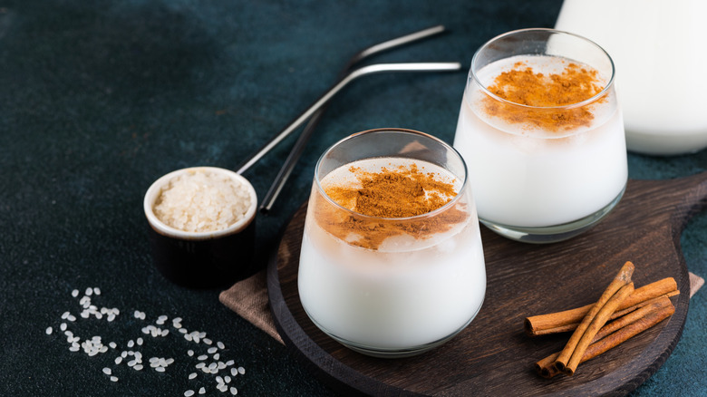 Two horchata cocktails on a cutting board with cinnamon sticks