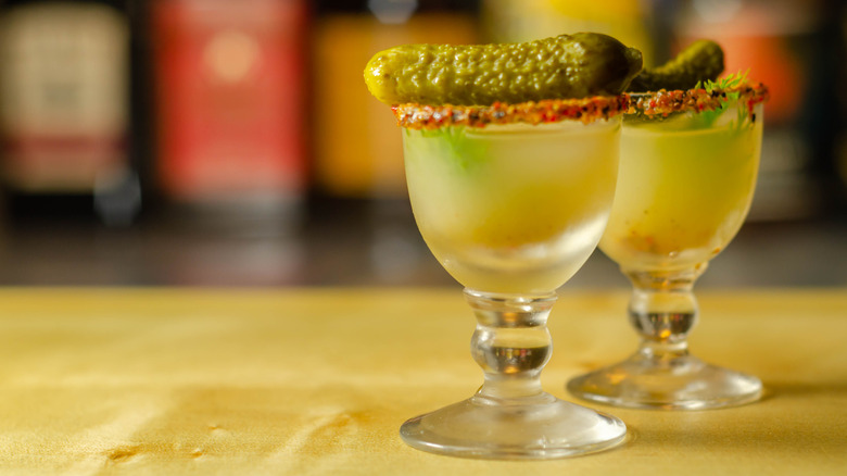 Two pickle juice shots on a bar with gherkins on top