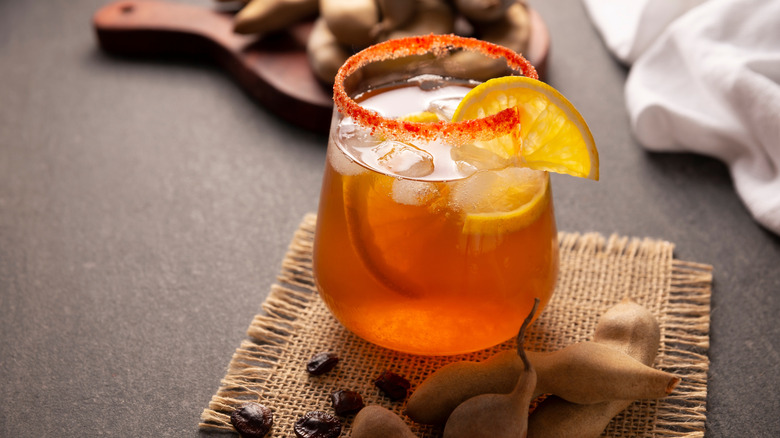 A tamarind cocktail garnished with lemon with tamarind pods at the forefront
