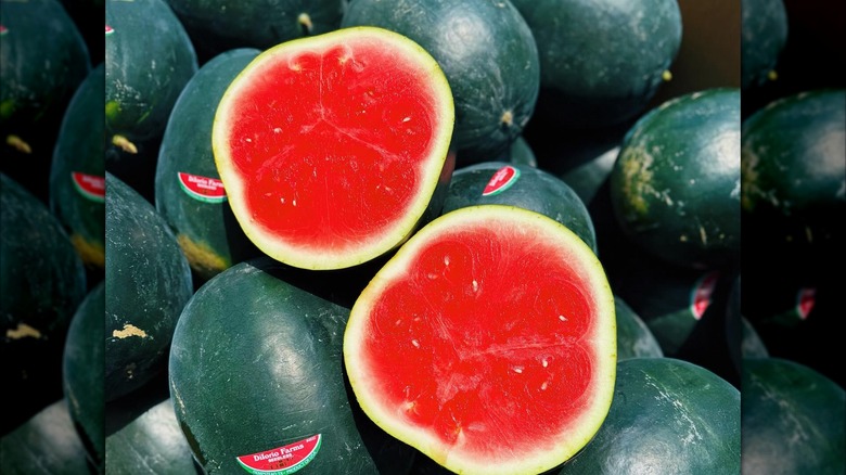 A pile of Black Diamond Seedless Watermelons with one cut in half at the top