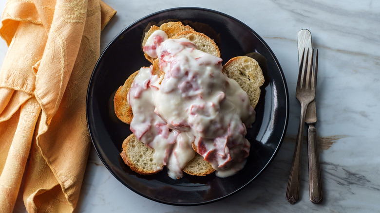 A plate of creamed chipped beef on toast set on a marble surface with cutlery nearby