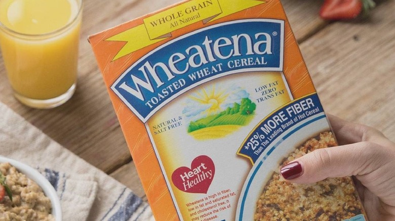 A person holding a box of Wheatena cereal with a breakfast table in the background