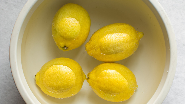 Four lemons submerged in a bowl of water