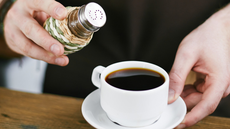 Barista sprinkling salt into a cup of black coffee