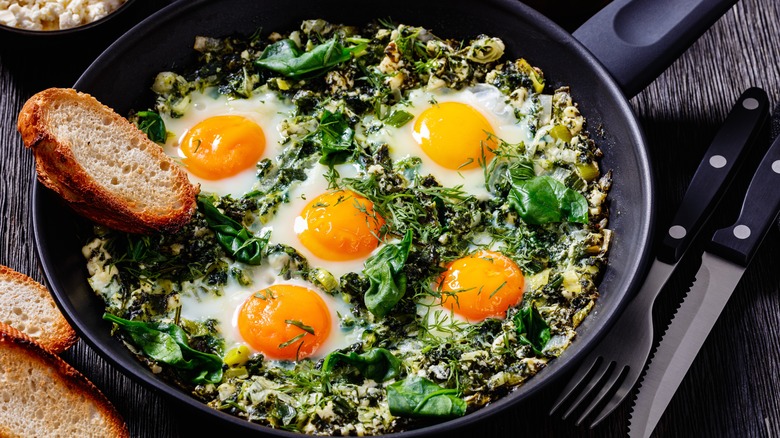 Green shakshuka in a frying pan with a hunk of bread