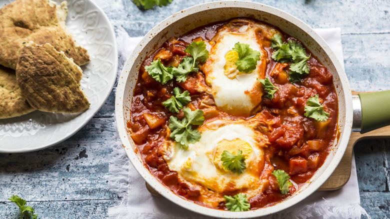 A sauté pan filled with shakshuka accompanied by some bread