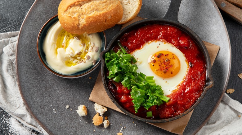 Spicy shakshuka in a small cast iron pan with bread and hummus