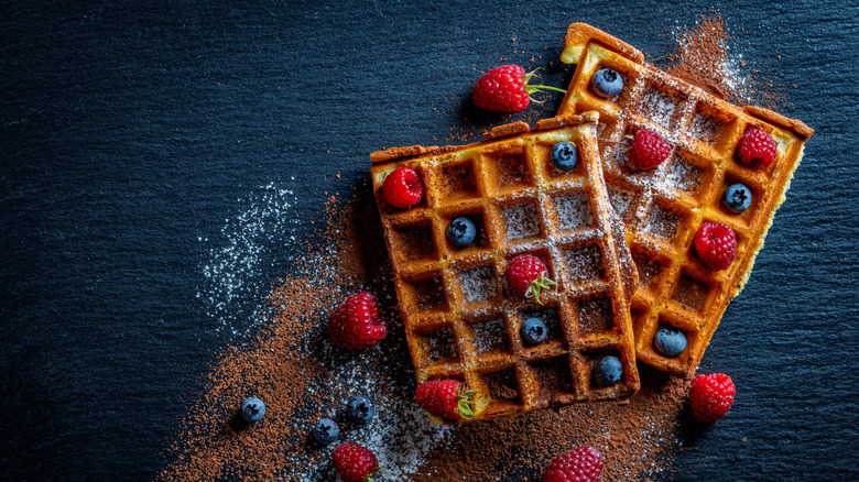 Two homemade waffles topped with berries and powdered sugar
