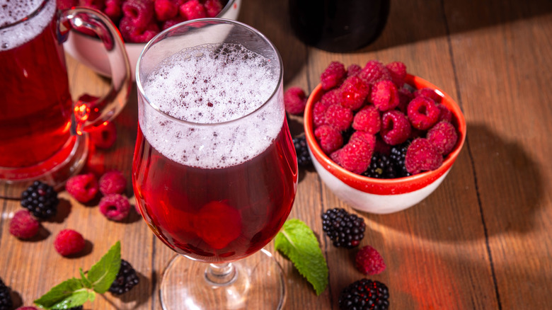 Fresh berry shandy in a hurricane glass surrounded by fresh berries in a bowl