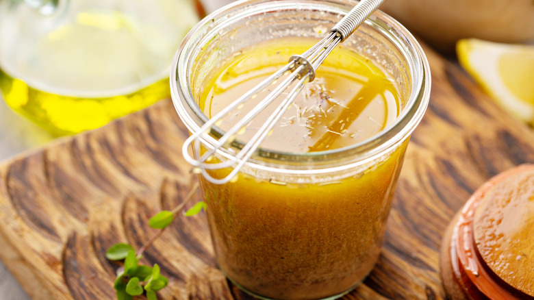 Glass jar filled with homemade salad dressing topped with a mini whisk