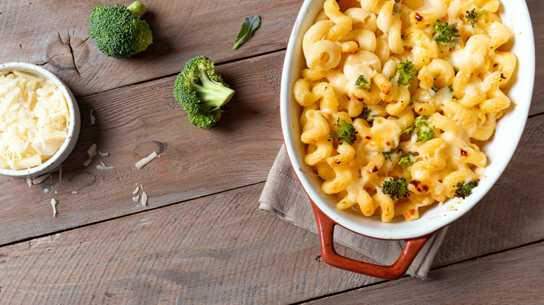 Dish of baked mac and cheese with broccoli and Parmesan cheese on wooden table