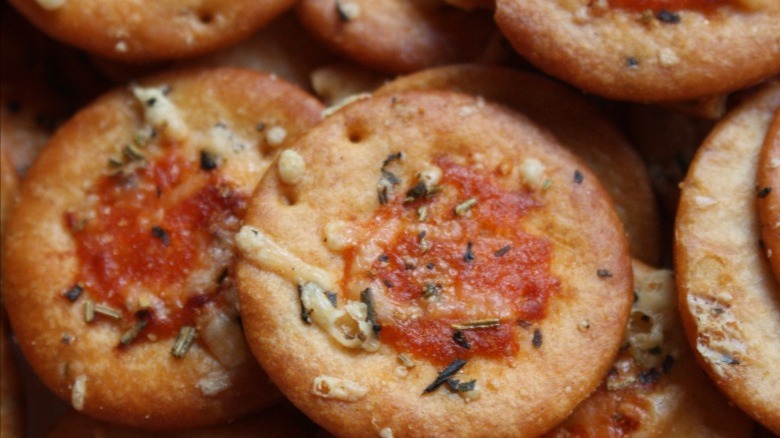 Crackers loaded with cheese, pizza sauce, and herbs