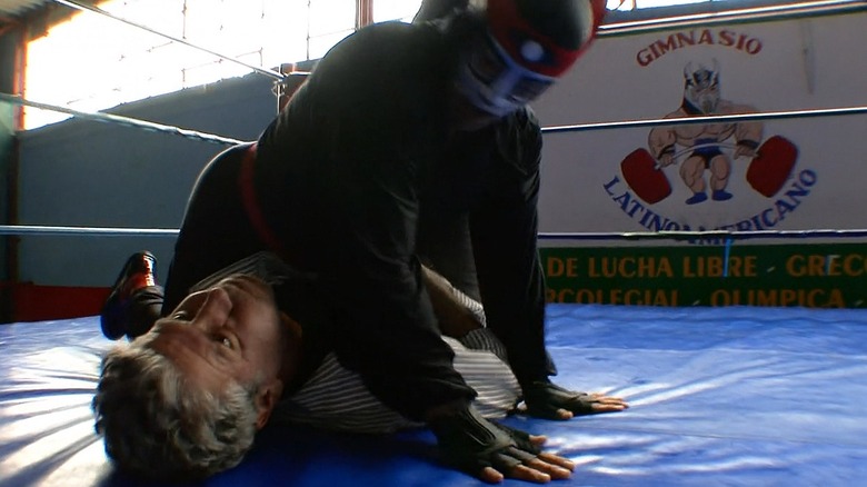 Anthony Bourdain in the lucha libre ring with El Octagón on top of him.