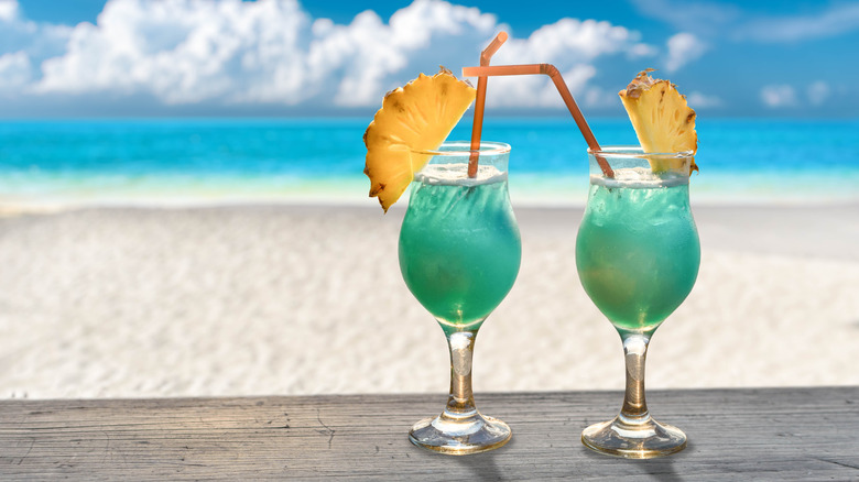 two blue Hawaiian on wooden table in front of a beach