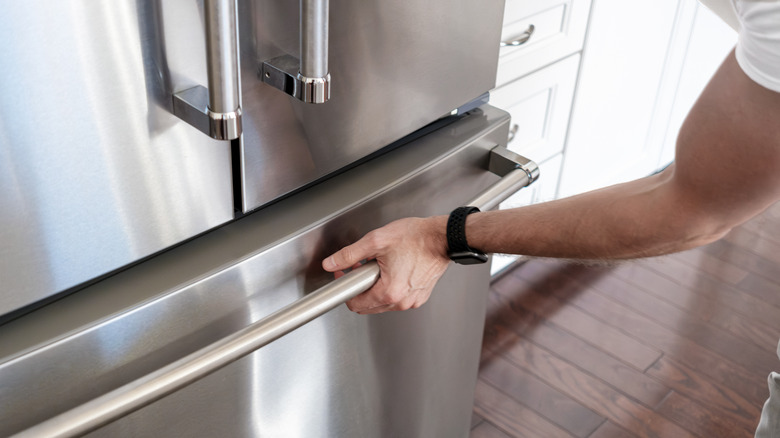 Man pulling on stainless steel freezer door located at bottom of appliance