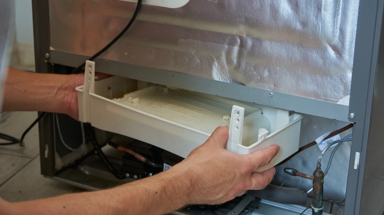 Person checks drip pan in back of refrigerator