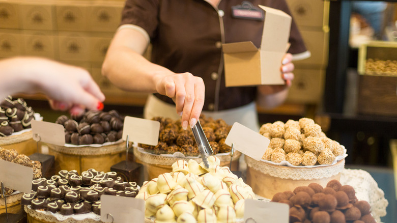 An employee at a candy store places chocolate truffles into a box