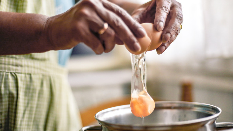 A person cracking an egg into a pot